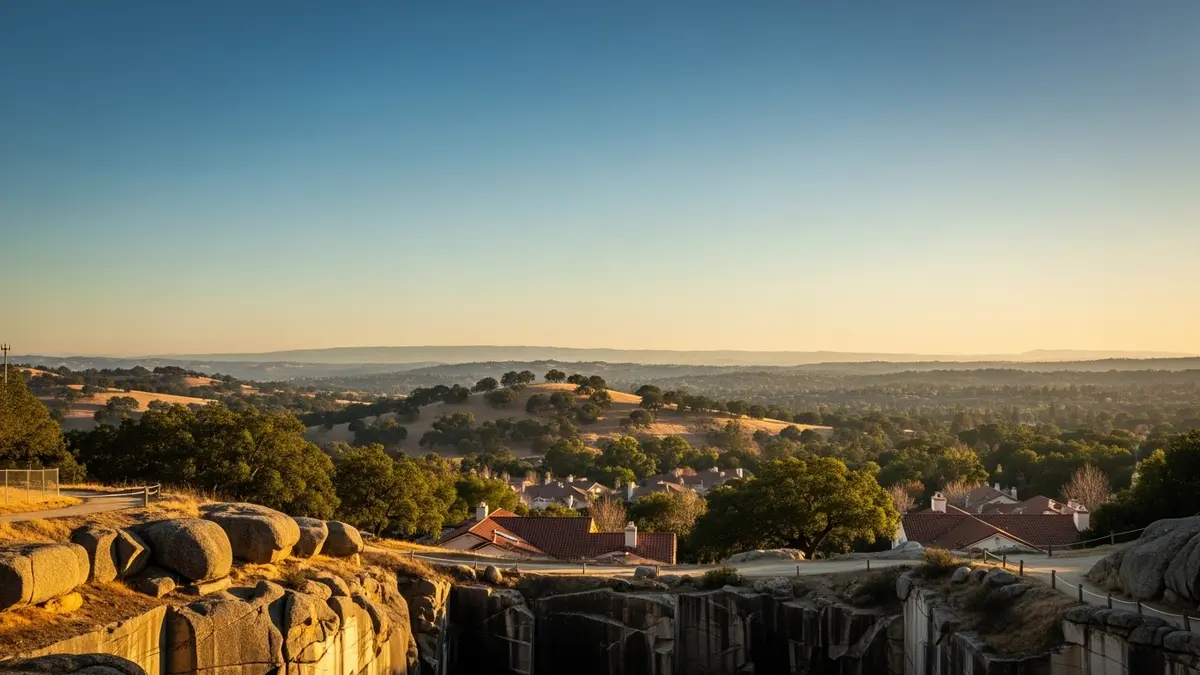 A scenic golden hour landscape of Rocklin, California, featuring distinctive granite outcroppings from Rocklin Quarry Park, rolling hills dotted with oak trees, and residential rooftops with warm terracotta tiles under a clear blue sky.