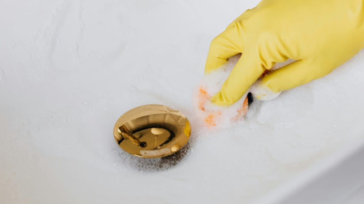 Person wearing yellow rubber glove cleaning a bathroom sink drain