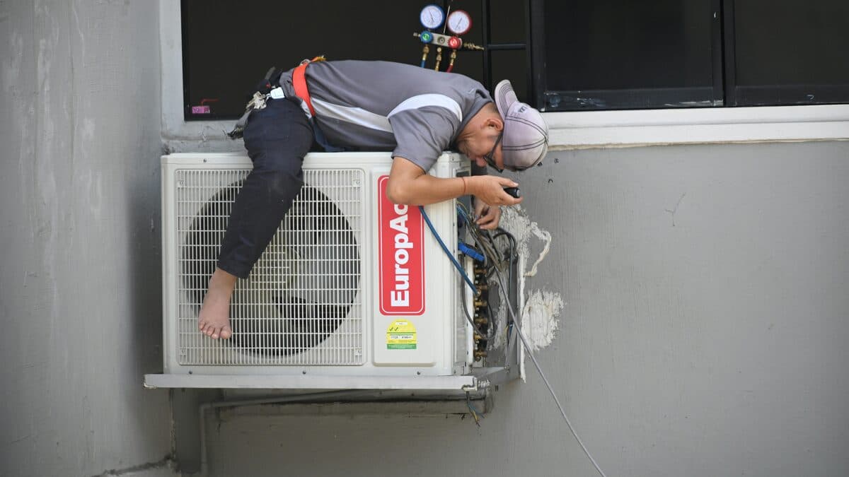 HVAC technician inspecting and repairing an outdoor air conditioning unit mounted on a building wall