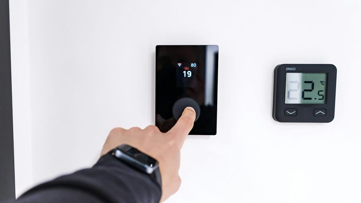 Hand adjusting a digital thermostat mounted on a wall in a modern home interior.
