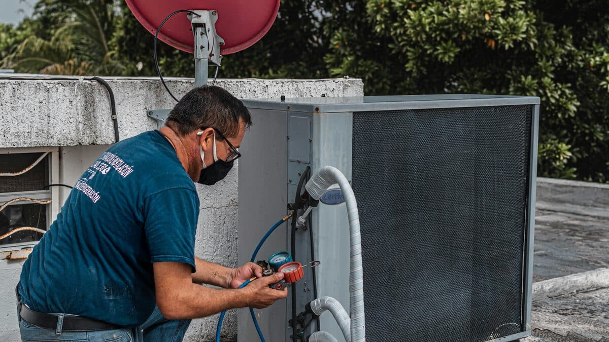 HVAC technician using a manifold gauge to check refrigerant on an outdoor AC unit